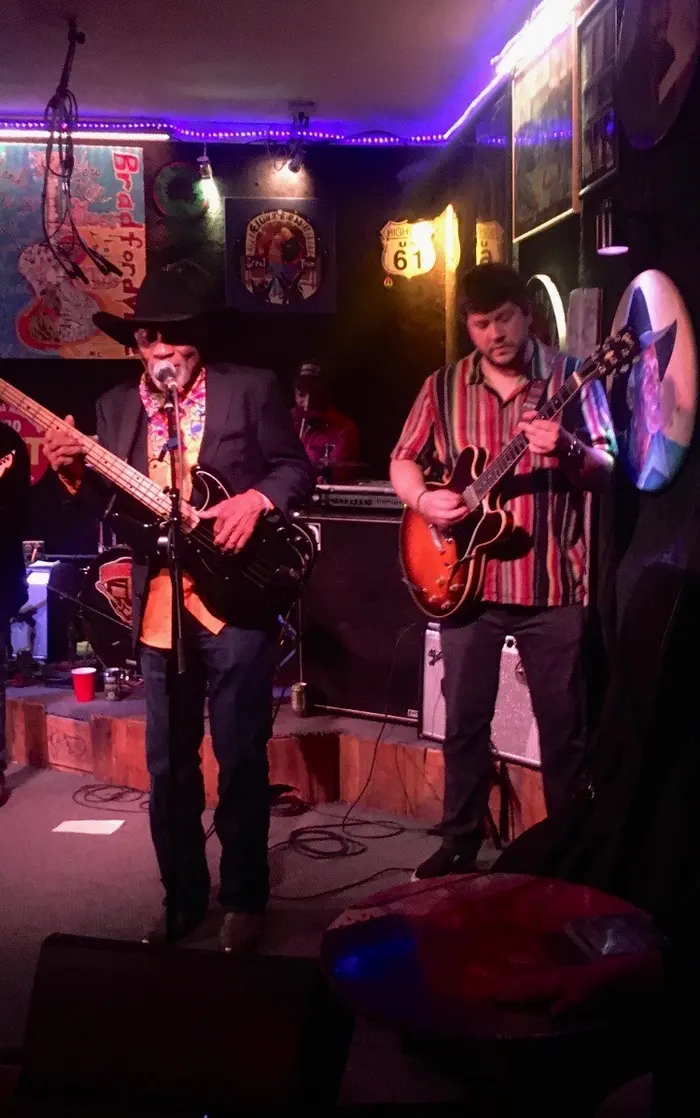 Johnny and a bandmate playing a small bar stage under purple lights
